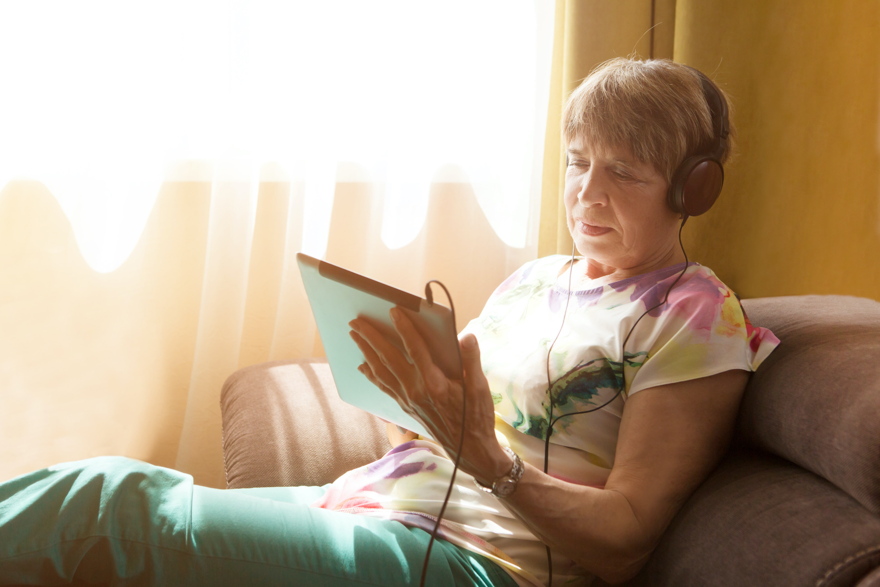 Senior woman in earphones using digital tablet at home.