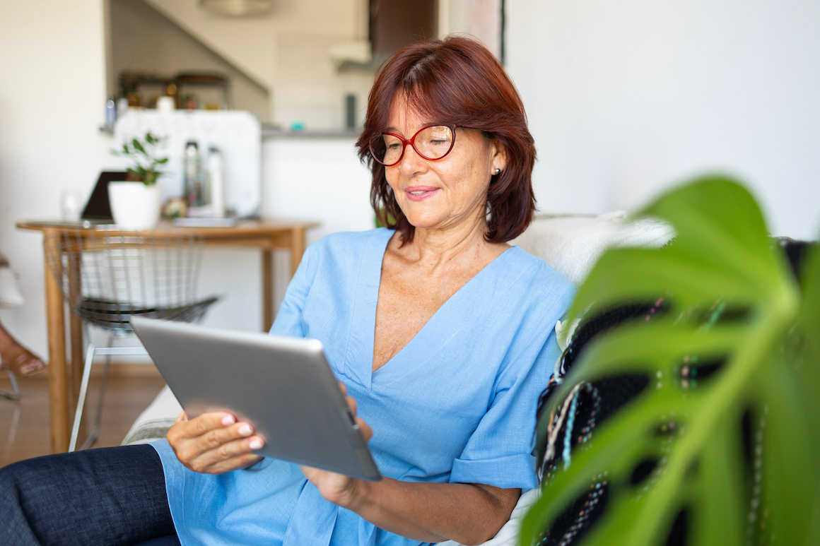 Mature latin Lady with glasses and light blue shirt using digital tablet in the apartment