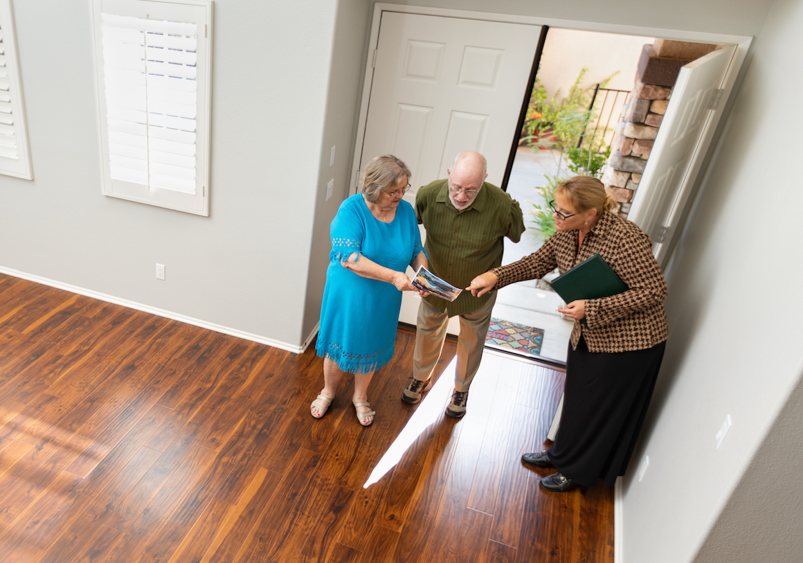 Female Real Estate Agent Showing Senior Adult Couple A New Home.