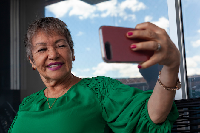older Latina woman in green blouse taking selfie with smartphone
