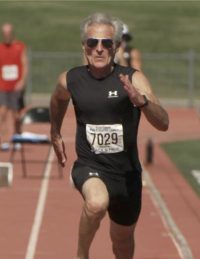 senior male in black athletic clothes running in track meet