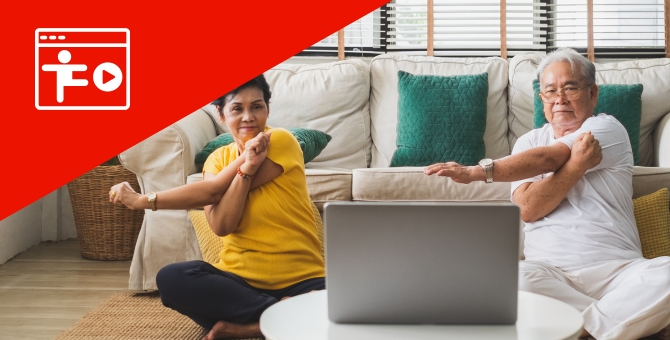 senior woman and man sitting on floor stretching while watching exercise class on computer