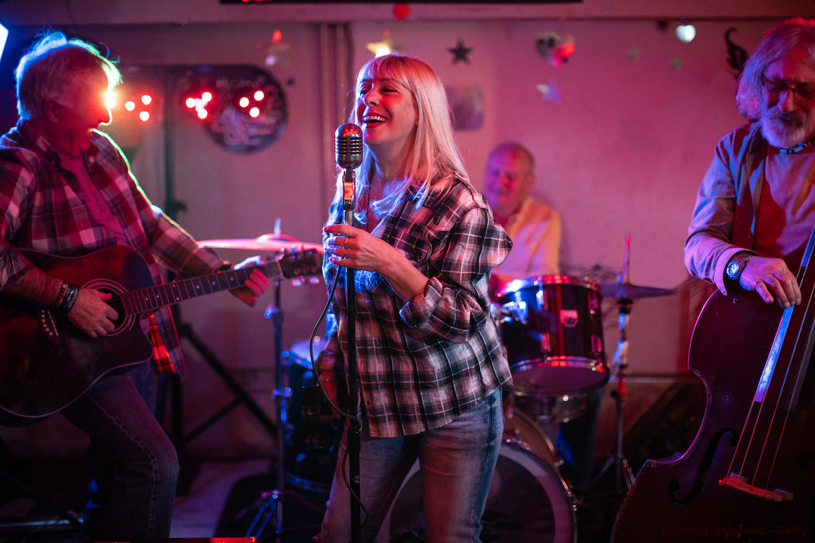 Senior woman with a microphone performing on stage with her band