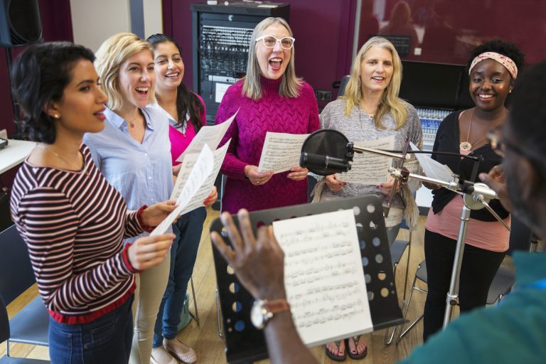 Male conductor leading womens choir with sheet music singing in music recording studio