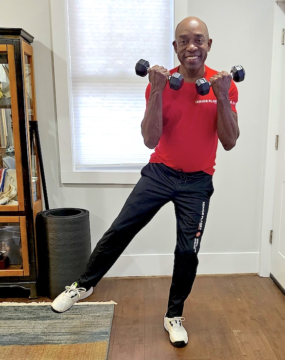 senior african american man exercising with weights, one leg raised