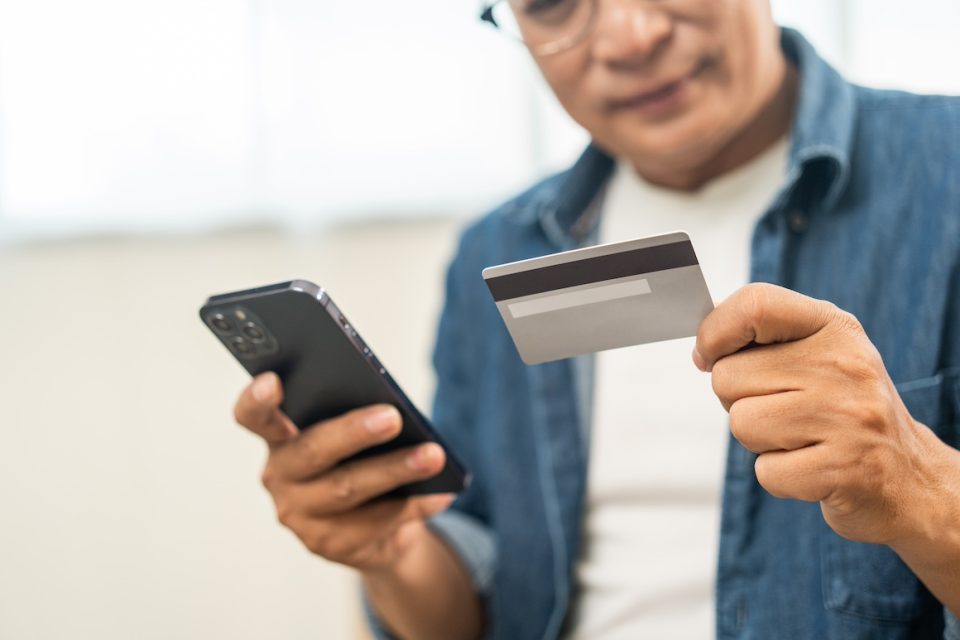 senior asian man holding credit card with smartphone for payment online.