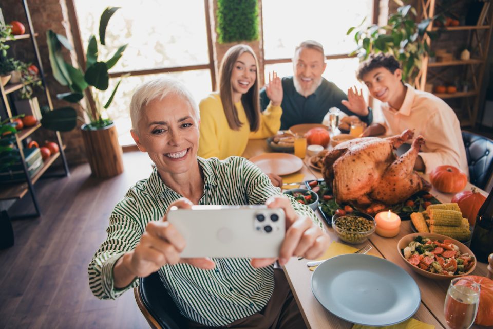 senior woman taking selfie around thanksgiving table with family