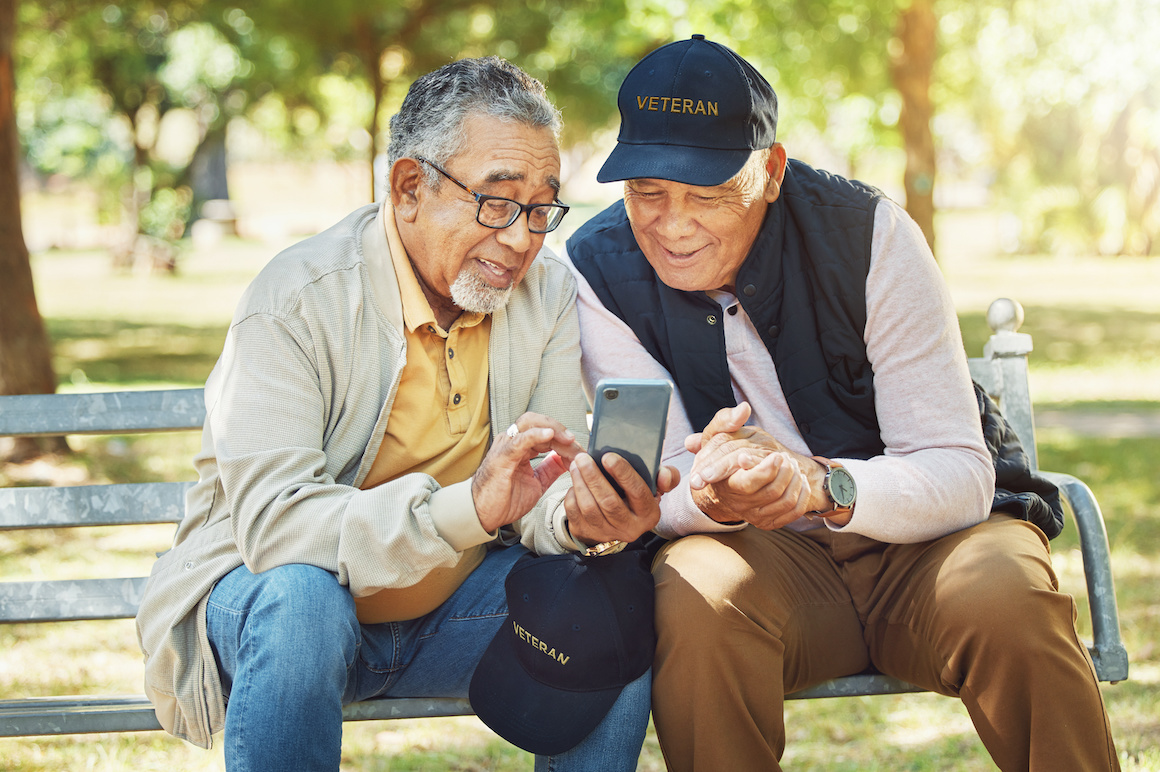 Senior military veterans sitting on bench talking and looking at smartphone