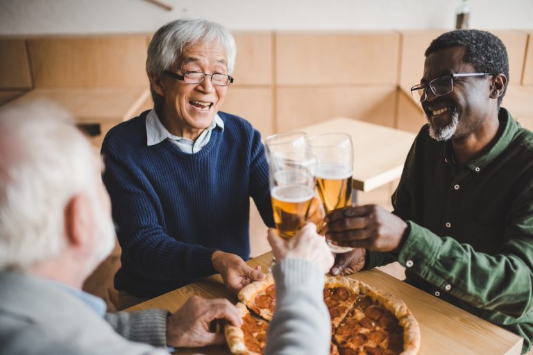 senior friends clinking glasses of beer and eating pizza