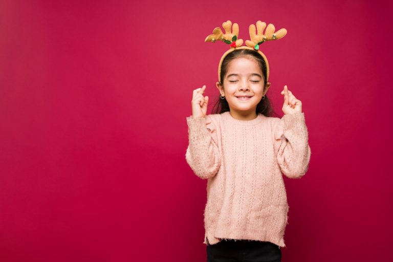 Little kid closing her eyes and making a christmas wish with her fingers crossed