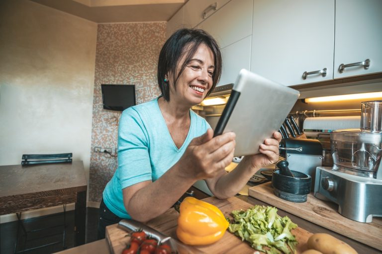 Senior woman cooking vegetables at home reading a recipe on a tablet