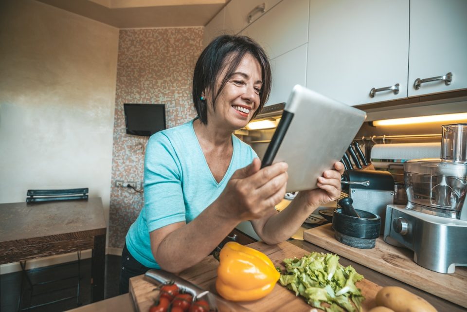 Senior woman cooking vegetables at home reading a recipe on a tablet