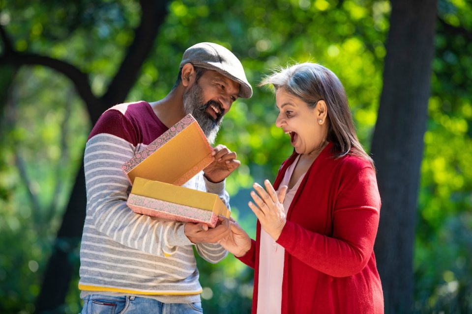 older Indian man giving surprise gift to older Indian woman at park