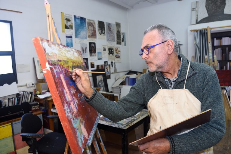 older artist painting a picture in the studio