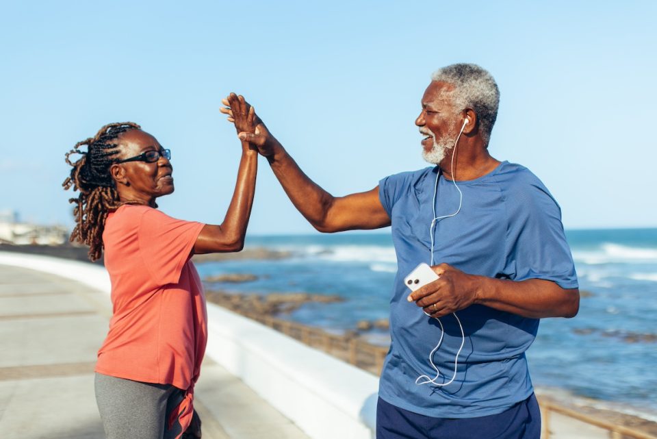 Senior couple celebrating fitness achievements with a high five by the seaside.