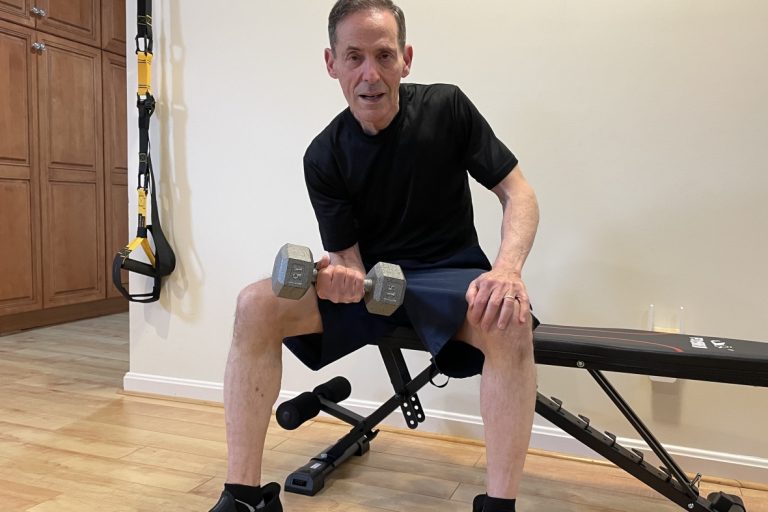 Man sitting on workout bench lifting dumbbell with right arm.