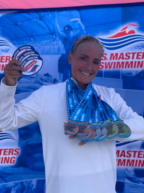 Woman holding up multiple medals from a swimming competition.