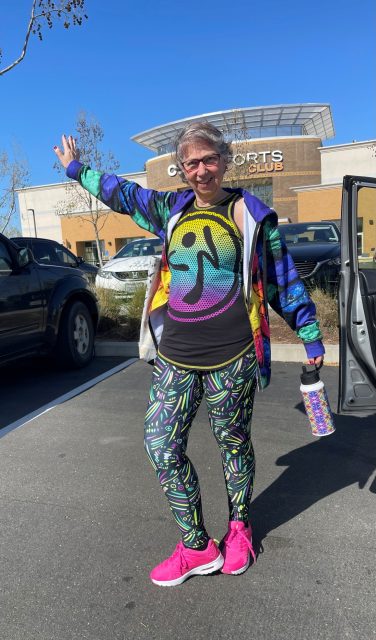 Woman in workout clothes in standing outside of a gym.