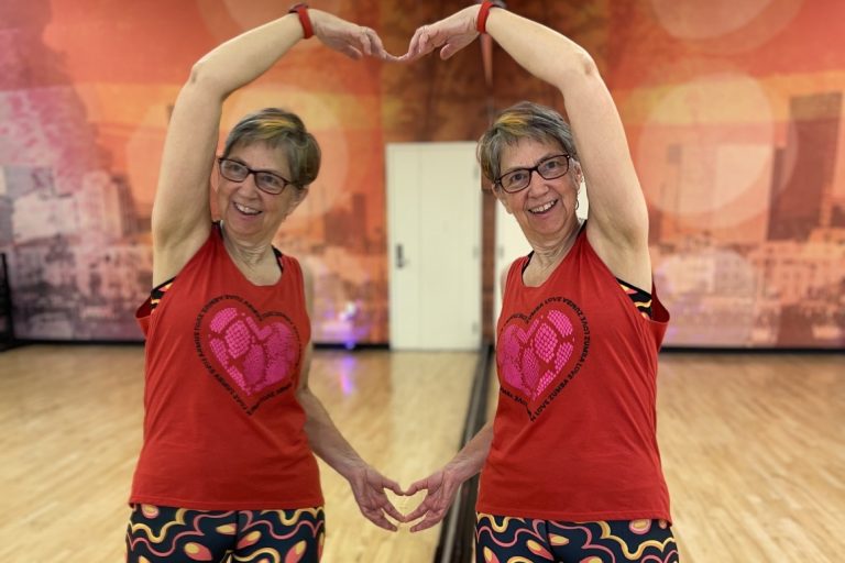 Woman in a exercise studio making a heart symbol with her arms and her reflection in the mirror.