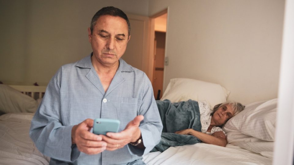 Man sitting in bed texting while his wife sleeps.