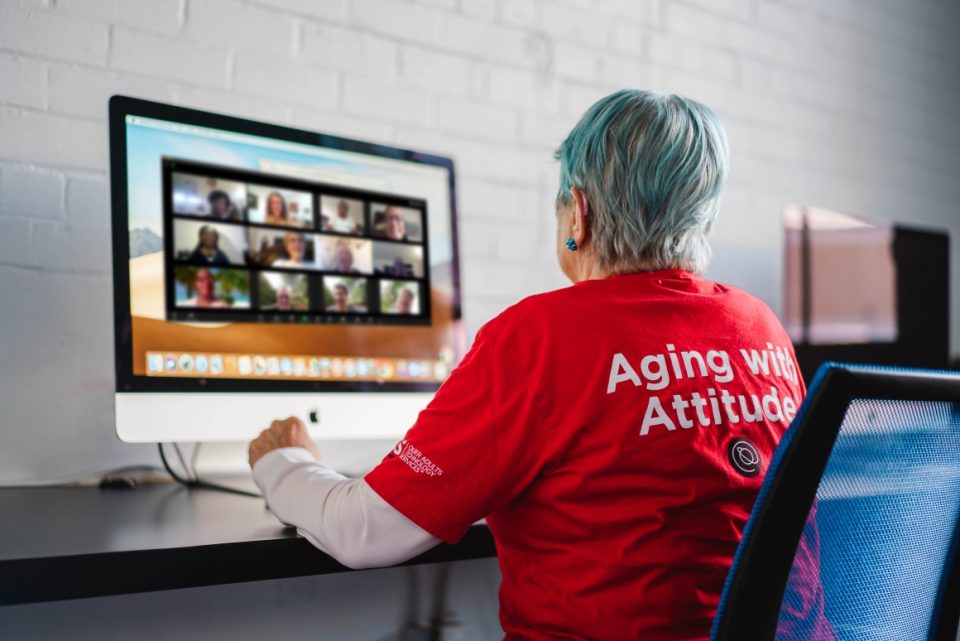 Senior woman in red t-shirt using computer on Zoom session with peers