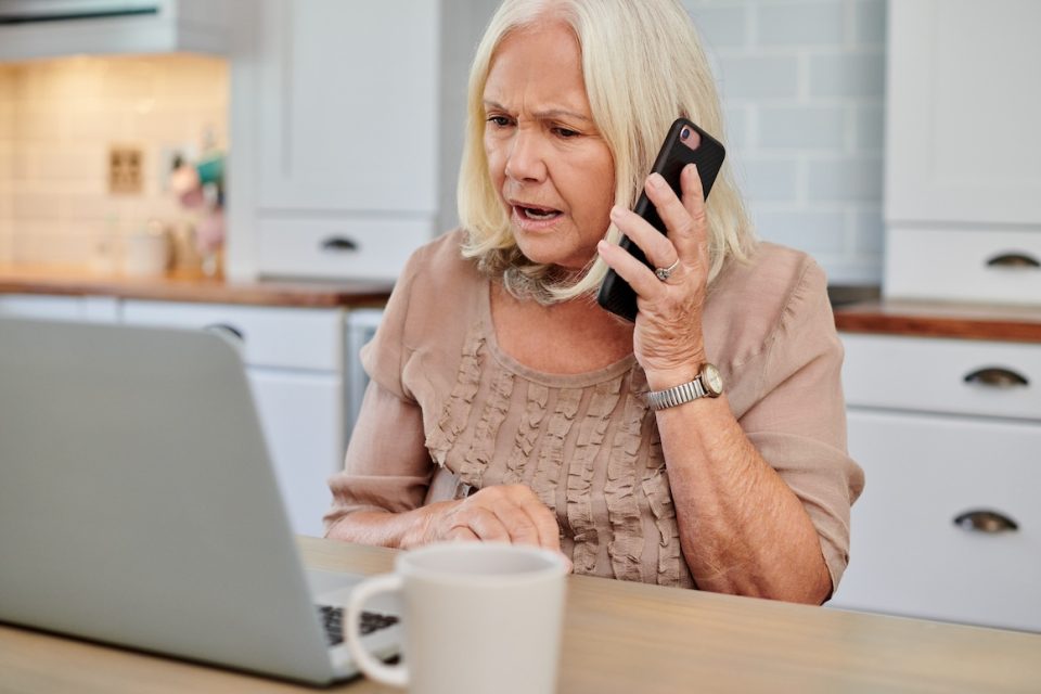 Shot of a senior woman looking concerned while using a smartphone and laptop at home