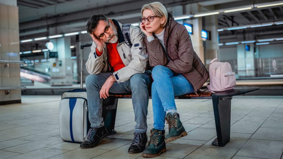 Traveling couple sitting on a bench at a train station showing visible frustration.