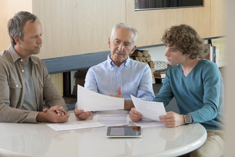 Senior man doing paperwork with son and grandson in a living room