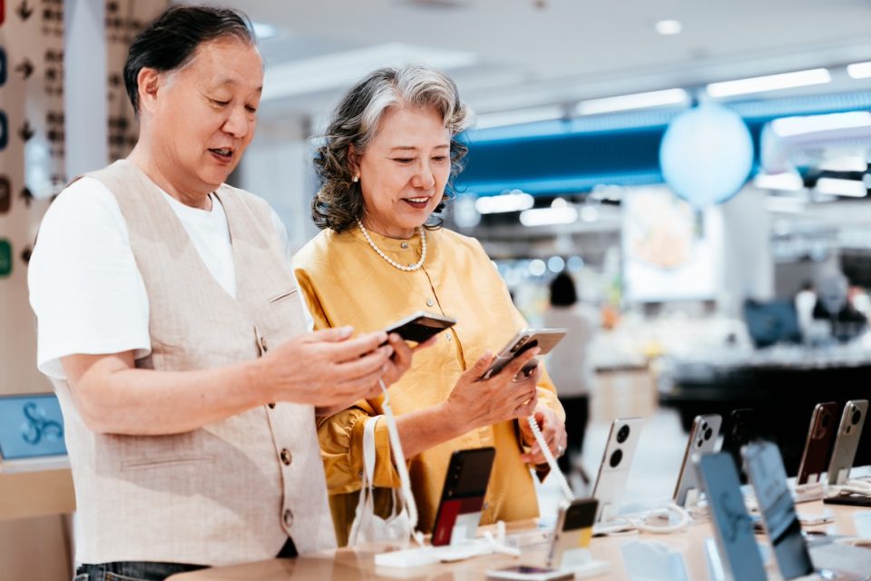 Asian senior couple using and selecting smartphone in modern electronics store.