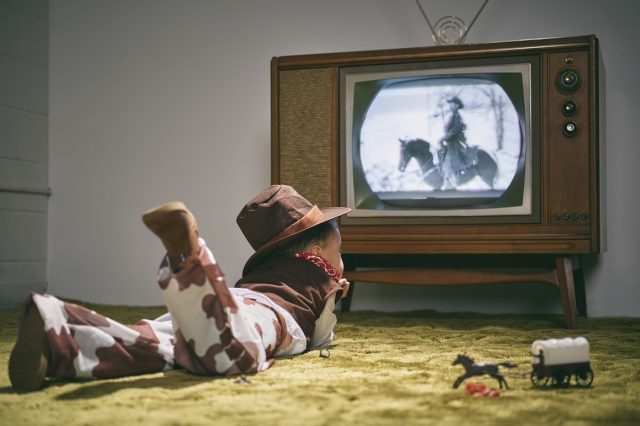 boy dressed as cowboy watching western on vintage tv set
