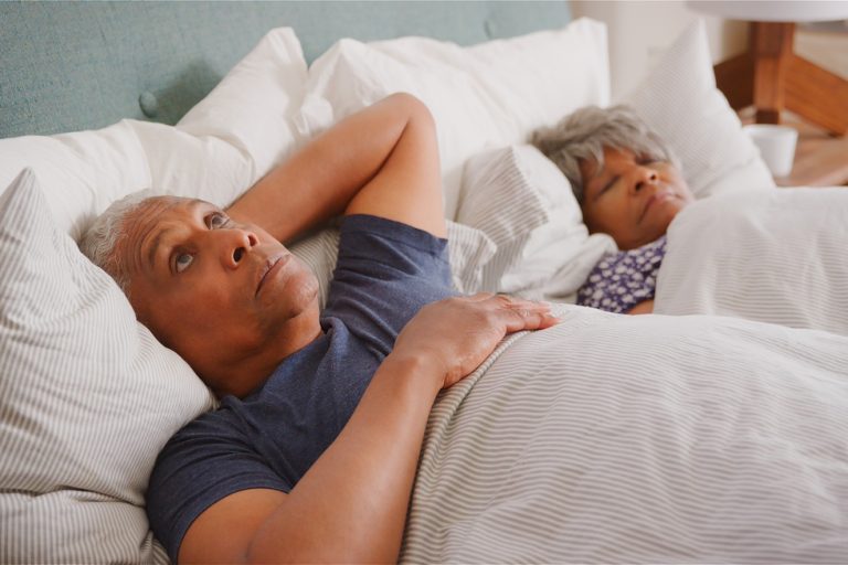 Worried Senior Man In Bed At Home Waking Up Next To Wife In Morning
