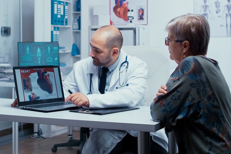 male doctor showing heart information to senior female patient on computer screen